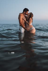 Un couple s’embrasse tendrement dans l’eau lors d’une séance grossesse au coucher du soleil, capturant l’amour et la complicité en bord de mer.