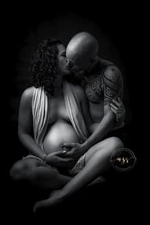Photographie en noir et blanc d'une femme enceinte assise en tailleur avec son mari l'embrassant en studio à Vergèze.