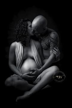 Photographie en noir et blanc d'une femme enceinte assise en tailleur avec son mari l'embrassant en studio à Vergèze.