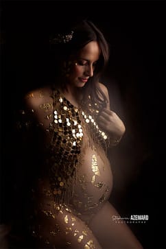 Femme enceinte parée d’ornements dorés et d’un bijou de corps, posant dans une ambiance douce et artistique. Photographie de maternité réalisée par Stéphanie Azemard à Montpellier.