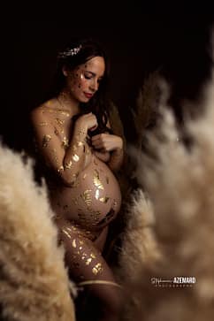 Femme enceinte posant dans un studio, le corps orné de feuilles d’or, entourée de pampas, dans une ambiance douce et artistique.