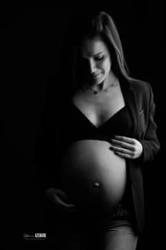 Portrait en noir et blanc d'une femme enceinte en clair-obscur, vêtue d'une veste et d'une brassière, photographiée en studio par Stéphanie Azemard à Montpellier.