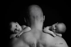 Portrait en noir et blanc d’un nouveau-né sur l’épaule de son père, illustrant un moment de tendresse.