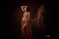 Femme enceinte en robe dorée scintillante posant avec un voile fluide en mouvement, photographie de maternité réalisée par Stéphanie Azemard à Montpellier.