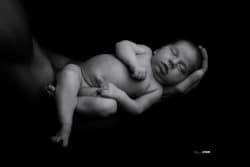 Nouveau-né paisiblement endormi dans les bras protecteurs de son père, en noir et blanc, capturant un moment de tendresse et de sécurité.