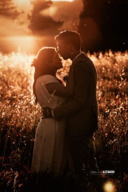 Un couple marié s'embrassant tendrement dans un champ baigné par la lumière dorée du coucher de soleil, capturé par Azemard Stéphanie, photographe à Montpellier.