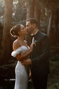 Un couple de mariés s’embrassant tendrement dans une forêt baignée de lumière douce, capturé lors de leur séance photo de mariage par Stéphanie Azemard, photographe à Montpellier.