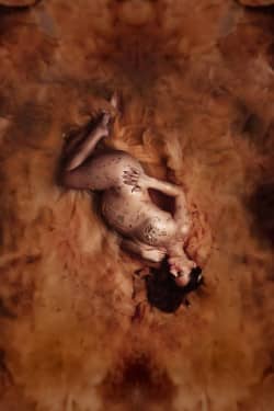 Femme enceinte allongée sur un voile doré, le corps délicatement orné de feuilles d’or, dans une ambiance artistique et chaleureuse. Son regard apaisé reflète la douceur et la magie de la maternité.