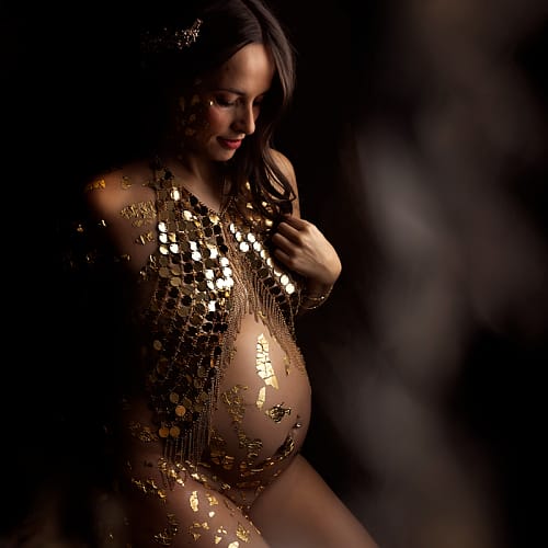 photo de maternite en studio par meilleur photographe azemard stephanie de montpellier Femme enceinte posant dans un décor sombre, vêtue d’une tenue artistique ornée de dorures et de feuilles d’or, éclairée en clair-obscur. Photo par Stéphanie Azemard à Montpellier.
